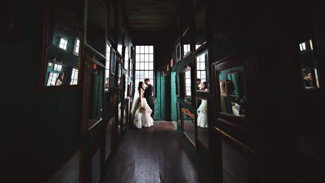 Bride and groom kiss in a mirrored hallway
